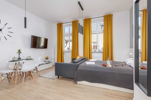 Ein modernes Schlafzimmer mit Bett, Fernseher, Schreibtisch und Essbereich.