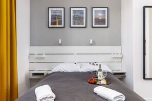 Een net opgemaakt bed met een dienblad met eten en drinken, een wit hoofdeinde en drie ingekaderde foto's aan de muur.