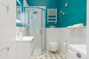 Ein modernes Badezimmer mit einer gläsernen Duschkabine, einer weißen Toilette und einem Waschbecken inklusive Spiegel.