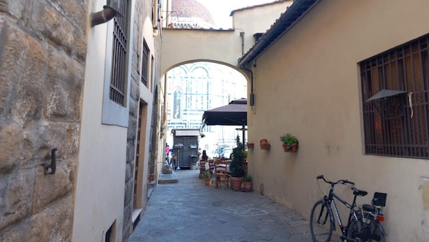 A narrow alleyway with stone walls, a bicycle, and a building with a tiled roof.