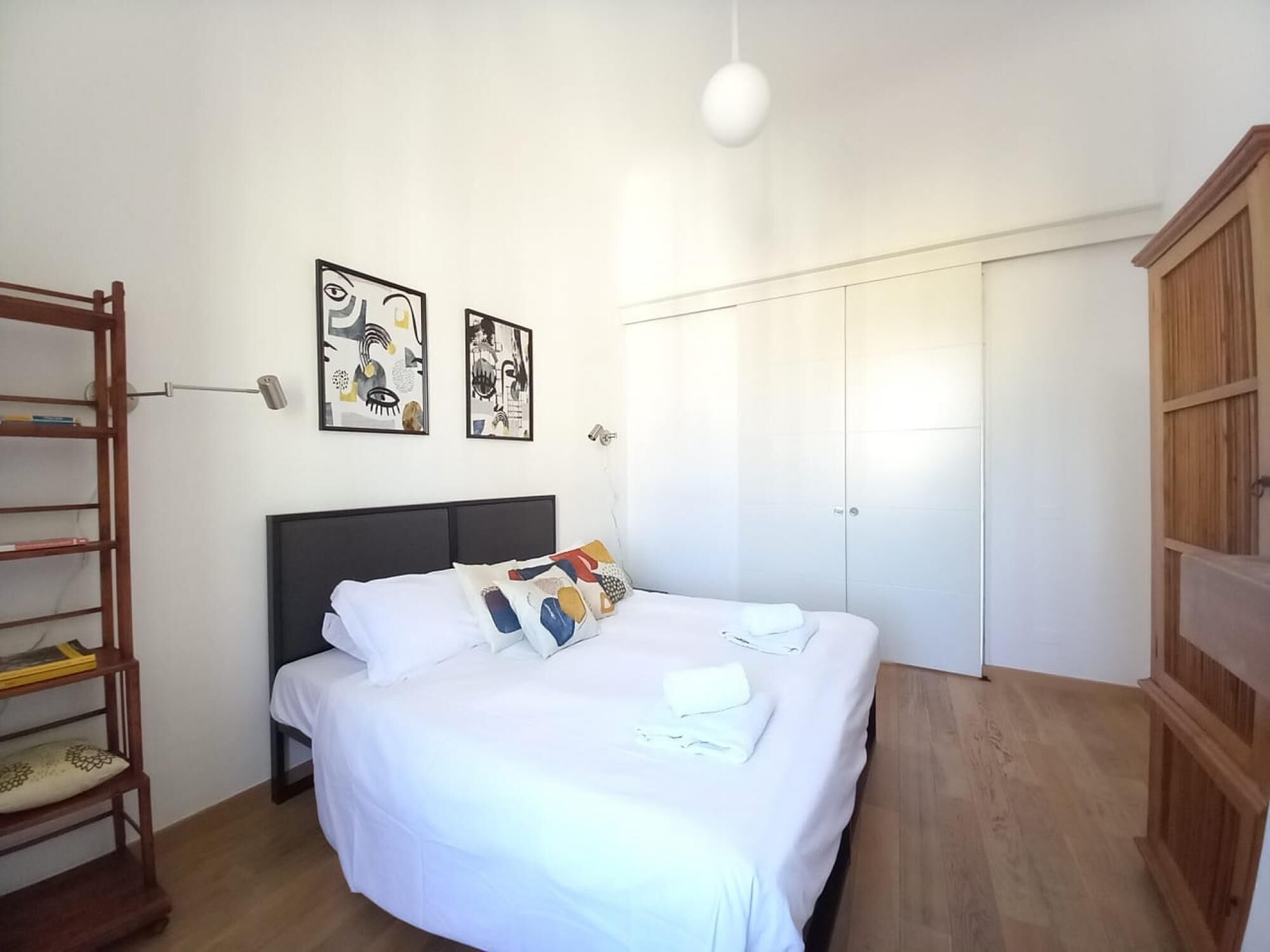 A bedroom with a bed, a wooden wardrobe, a desk, and a chair.