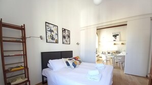 A bedroom with a bed, a wooden ladder, and two framed artworks on the wall.
