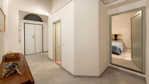 A hallway with a wooden bench, a wicker basket, and a door leading to a bedroom with a bed and a nightstand. - San Zanobi 33 in Firenze (Florence)