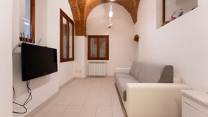 A narrow hallway with a tiled floor, a white sofa, a television mounted on the wall, and a radiator. - San Zanobi 33 in Firenze (Florence)