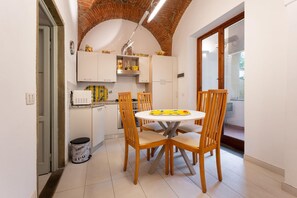Una cocina compacta con armarios blancos, una mesa redonda de comedor con sillas de madera y techo de ladrillo.