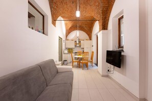 Una sala de estar moderna con un sofá gris, un comedor con sillas de madera y una cocina con armarios blancos.