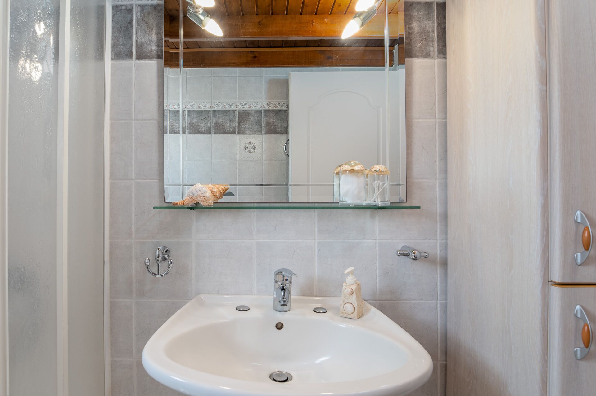 Een badkamer met een wit wastafel, een spiegel erboven en een plank met decoratieve objecten.
