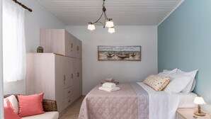 Una camera da letto con un letto, un comodino, un divano in vimini, un armadio e un quadro appeso al muro.