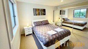 A modern bedroom with a large bed, bedside tables, a mirror, and artwork on the wall. - Beige & Beautiful - Close to ANU (Turner)