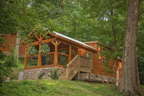 Une cabane en rondins dotée d’une véranda, de fondations en pierre et d’un escalier menant à l’entrée.