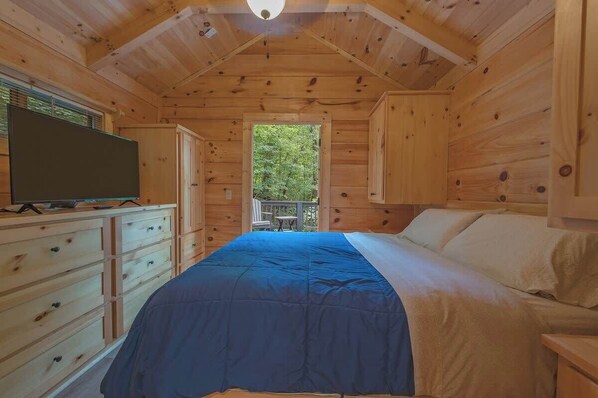 Un dormitorio de cabaña de madera con cama, cómoda y televisor.