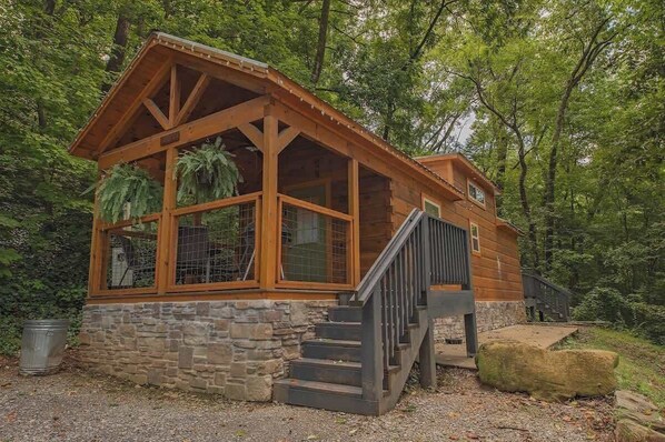 A wooden cabin with a stone foundation, large windows, and a staircase leading to a deck.