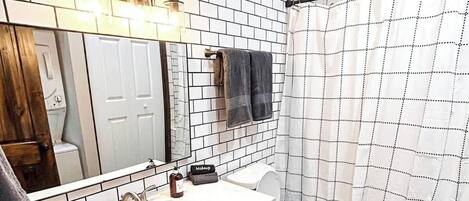 Un baño con pared de azulejos blancos, tocador verde, inodoro blanco y cortina de ducha.