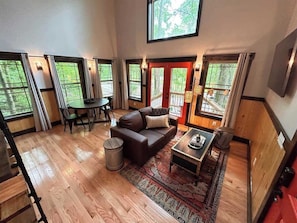 A spacious living room with a wooden floor, a brown sofa, a coffee table, and a dining area with a table and chairs.