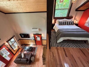 A room with a bed, a sofa, a small table, a red door, and a window.