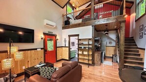 Ein geräumiger Wohnbereich mit hoher Decke, eine Treppe zu einer oberen Ebene sowie eine durchgehende Tür erkennbare Küchenzeile.
