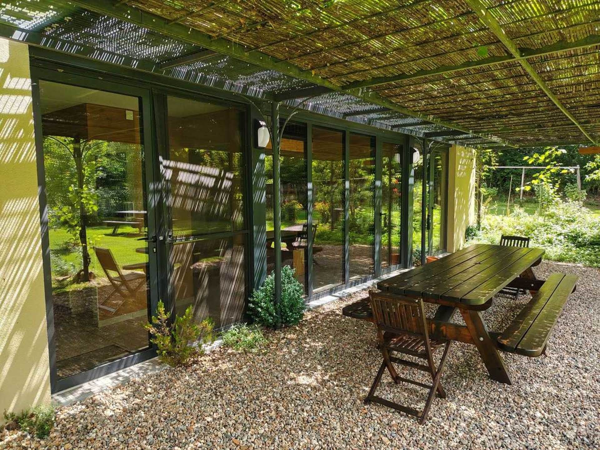 Un espace extérieur abrité, aménagé pour les repas, avec une table et des chaises, entouré de portes vitrées et offrant une vue sur un jardin.