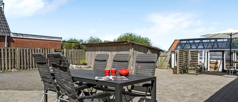 Une terrasse avec une table et des chaises, une clôture en bois et un bâtiment doté d’un toit en pente.
