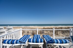 Una terraza con barandillas blancas y sillones reclinables a rayas azules, orientada hacia la playa.