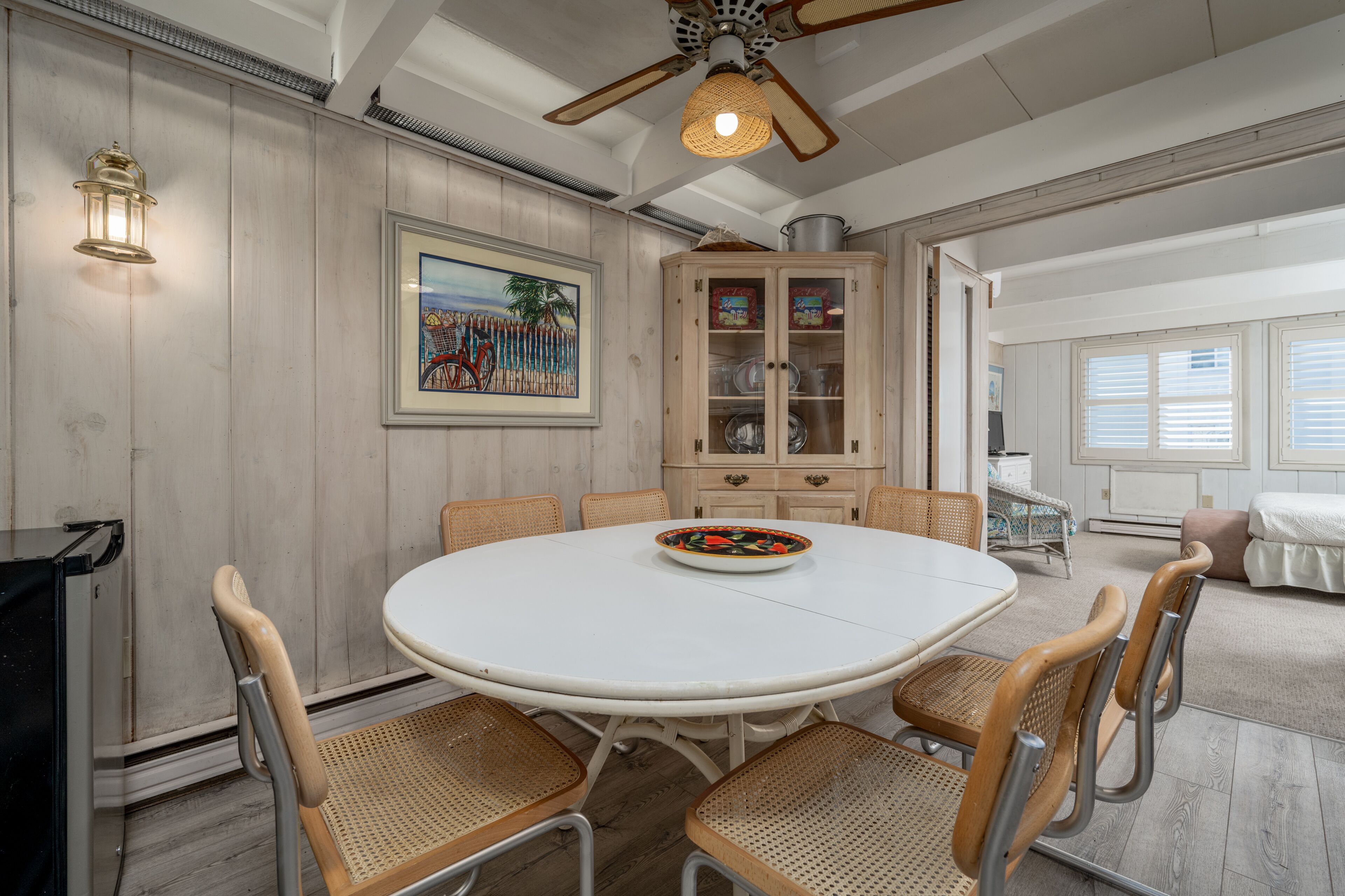 A dining area with a round table, six chairs, a cabinet with glass doors, and a ceiling fan.