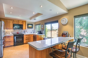 A kitchen with wooden cabinets, a stainless steel refrigerator, a black stove, and a large island with bar stools.