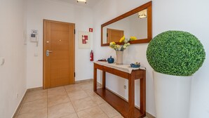 En gang med en trædør, et konsolbord med en vase blomster, en rund, grøn plante og et spejl på væggen.