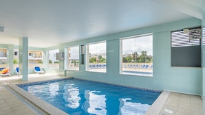 En indendørs swimmingpool med krystalklart, blåt vand, store vinduer og udsigt over bybilledet.