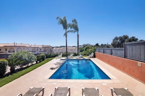 Une piscine rectangulaire à l’eau d’un bleu limpide, entourée d’une terrasse carrelée agrémentée de chaises longues.