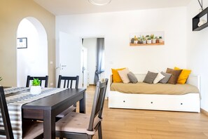 Ett modernt vardagsrum med en soffa, ett matbord, stolar och ett köksområde i bakgrunden.