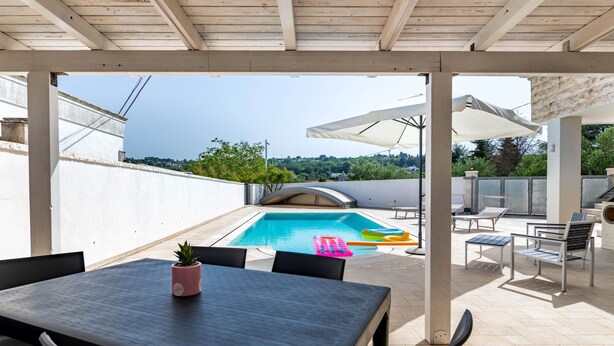 Ein überdachter Außenbereich mit Pool, Sitzgelegenheiten und Blick auf die Landschaft.