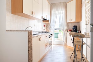 Une cuisine avec des meubles blancs, un plan de travail en granit, un évier et un tabouret de bar.