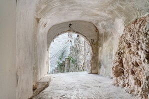 Ein gewölbter Steinkorridor mit einer Treppe, die zu einer höheren Ebene führt, und einem Metallgeländer entlang der Wand.