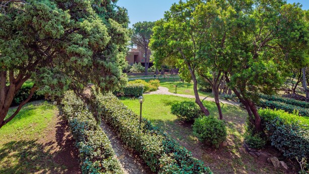 Ein angelegter Garten mit Wegen, Bäumen und einem Gebäude im Hintergrund.