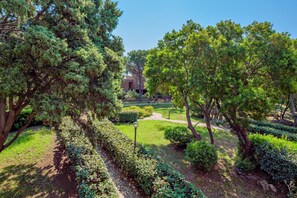 A landscaped garden with pathways, trees, and a building in the background. - Holiday Home 'Libeccio 2417' with Shared Pool, Private Terrace and Balcony (Cugnana)
