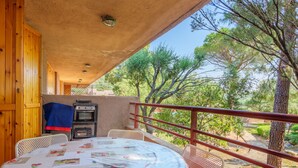Un espace extérieur abrité, aménagé pour les repas, avec une table pour deux, un barbecue et une vue sur les arbres.