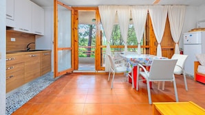 Une pièce comprenant une table à manger, des chaises, un ventilateur de plafond et un coin cuisine avec des placards et un réfrigérateur.