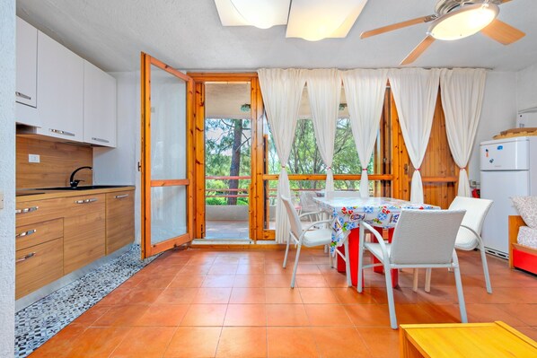 A room with a dining table, chairs, a ceiling fan, and a kitchen area with cabinets and a refrigerator.