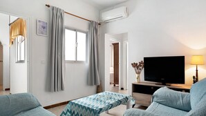 Ein Wohnzimmer mit Fernseher, Sofa und einem Tisch mit gemustertem Tischläufer.