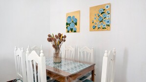 Ein Esstisch mit weißen Stühlen, eine Vase mit getrockneten Blumen und zwei Bilder an der Wand.