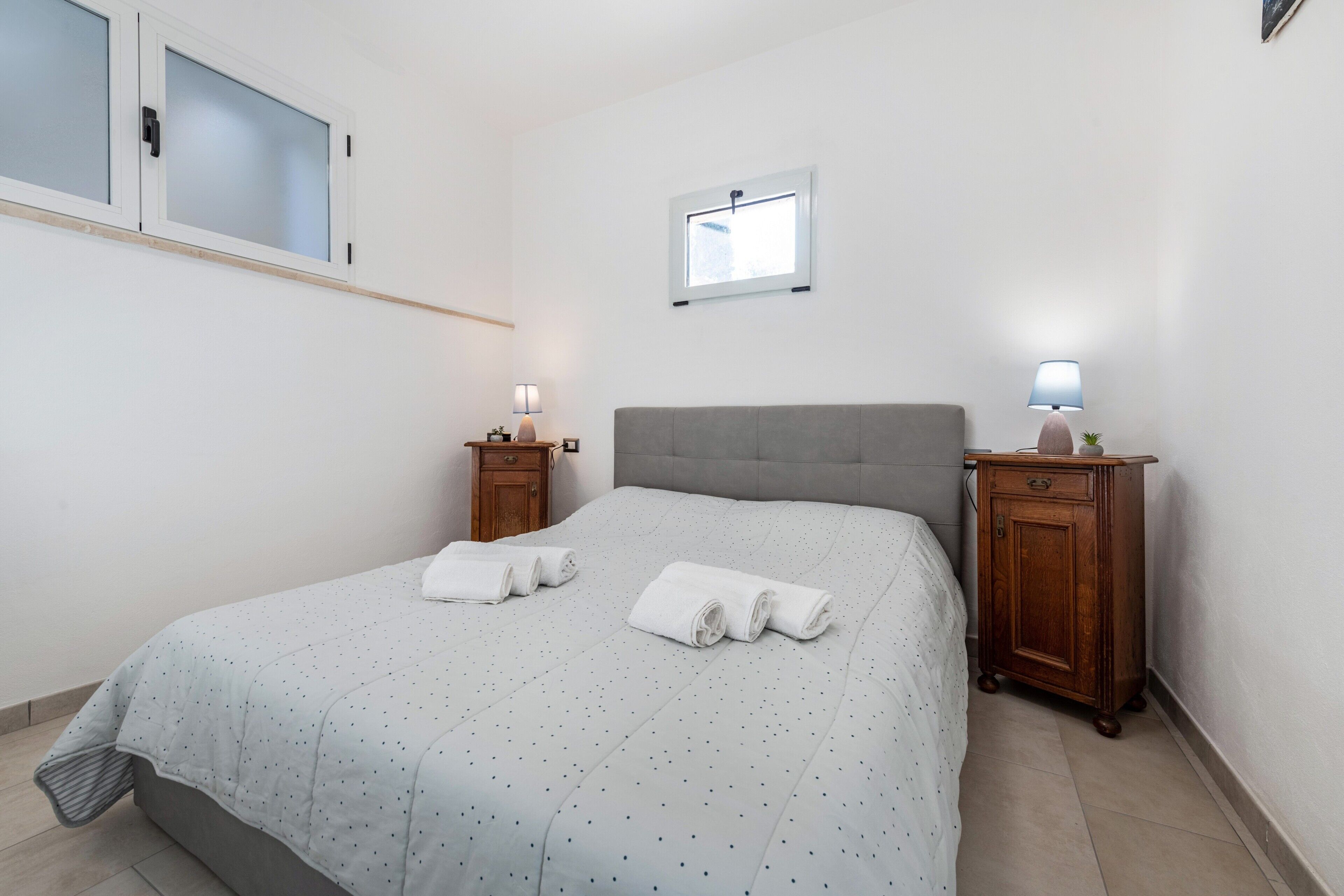 Una camera da letto con un letto, due comodini, una finestra e uno specchio fissato alla parete.