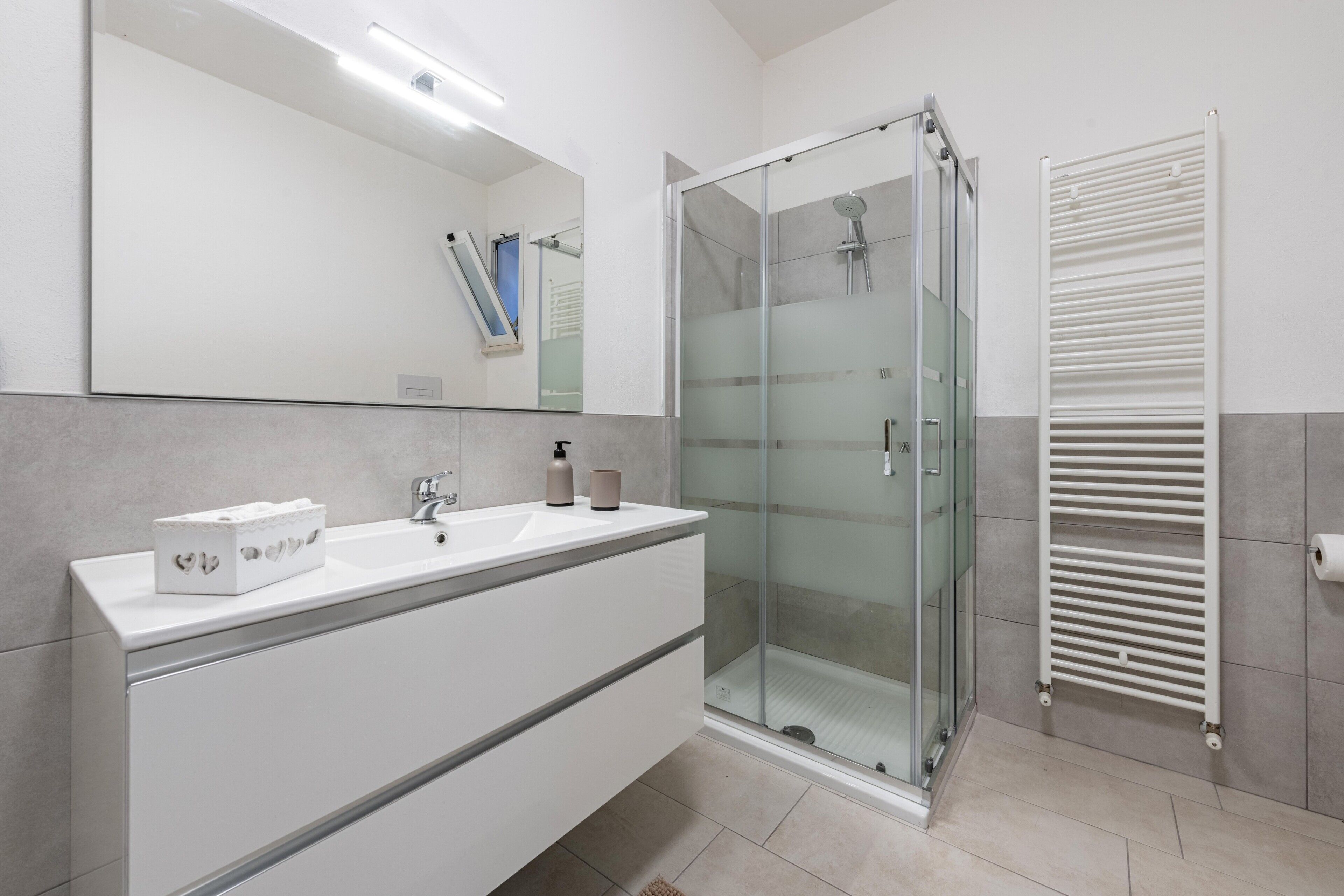 A modern bathroom with a glass shower enclosure, a white vanity with a mirror, and a towel rack.