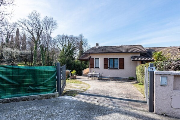 A two-story house with a tiled roof, a fenced yard, and a paved driveway.