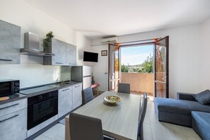 A modern kitchen with a dining area, a TV, and a balcony with a view.