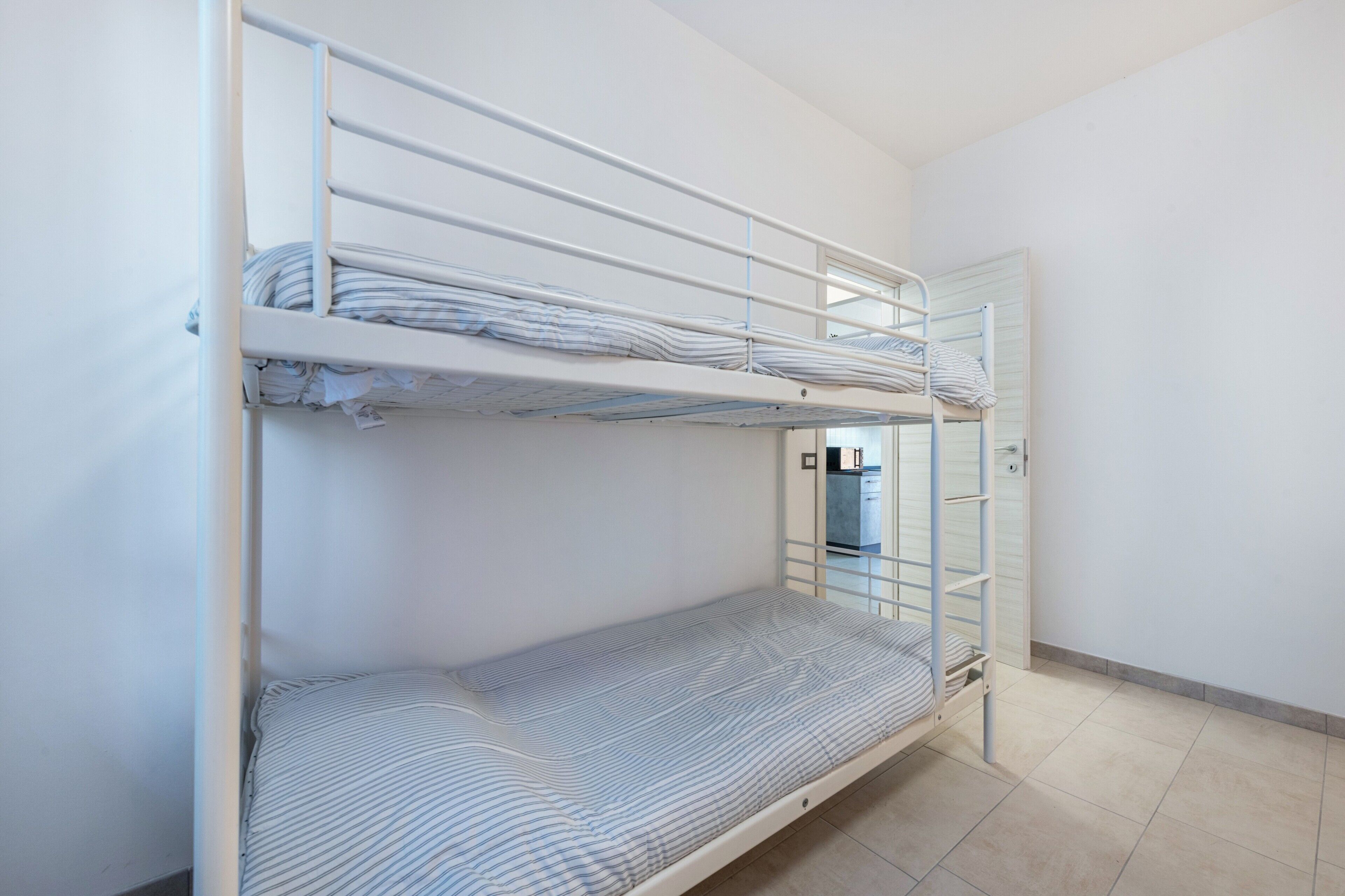 Un lit superposé avec une fenêtre, une porte et un sol carrelé.