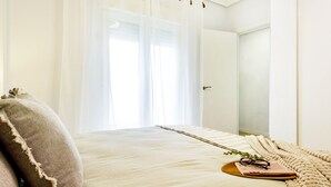 A bedroom with a bed, a bedside table with glasses and a book, and a window with sheer curtains. - Nice Apartment with Pool (Torrevieja)