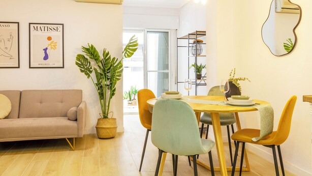 A modern living room with a beige sofa, a dining table with yellow chairs, and a large potted plant. - Nice Apartment with Pool (Torrevieja)