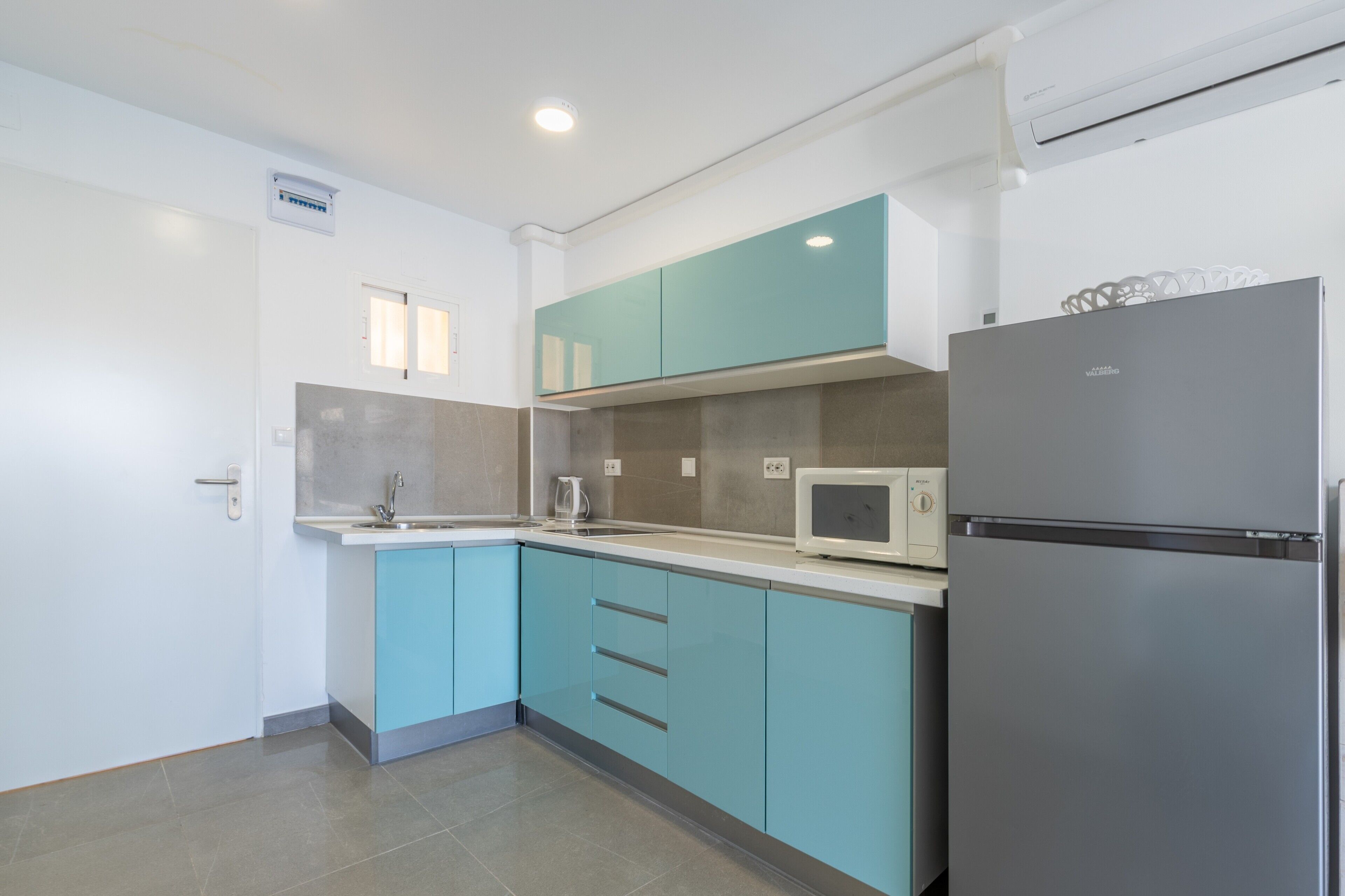 A modern kitchen with teal cabinets, a stainless steel refrigerator, and a microwave.