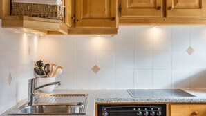 Eine Küche mit Spüle aus Edelstahl, einem eingebauten Backofen, Holzschränken und einer gefliesten Spritzschutzwand.