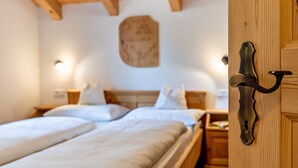 Ein Hotelzimmer mit Holzbalkendecke, einem Bett mit weißen Leinen, einem Nachttisch und einer wandmontierten Lampe.