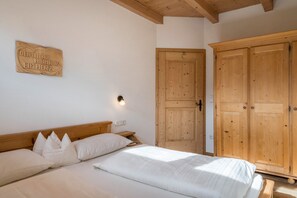 A bedroom with a wooden headboard, a bed with white bedding, a wooden wardrobe, and a wall-mounted light fixture.